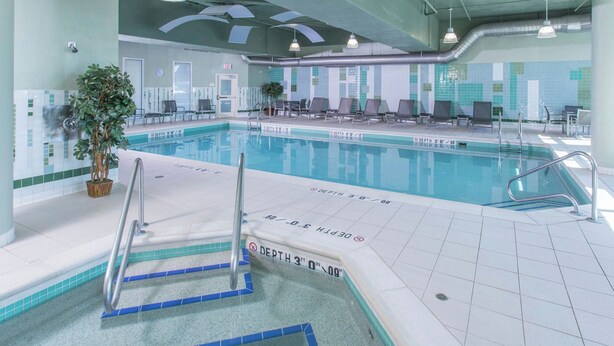 Una piscina interior con marcadores de profundidad visibles, sillas de descanso y una planta en maceta.