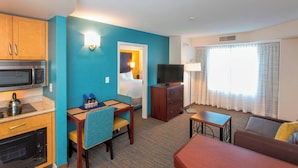 Una habitación de hotel compacta con kitchenette, zona de comedor, sala de estar y televisor.