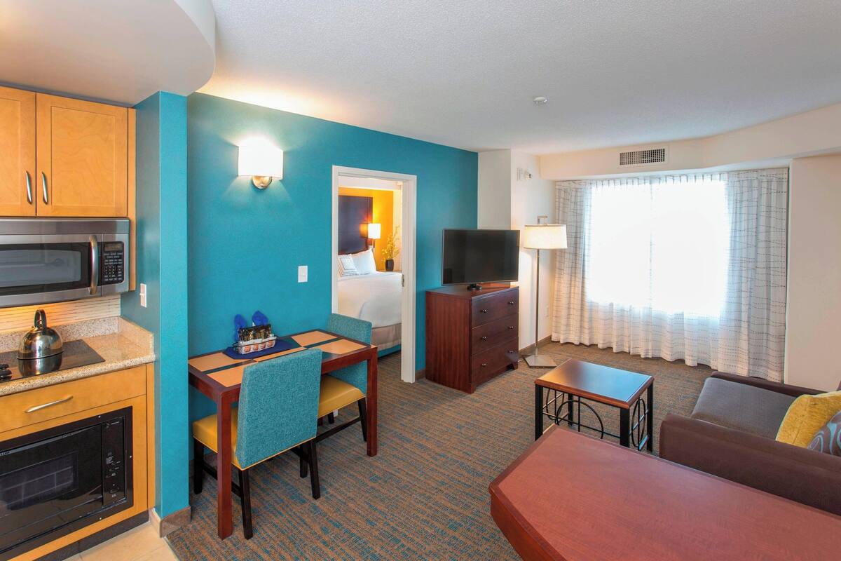 A compact hotel room with a kitchenette, a dining area, a living space, and a television.