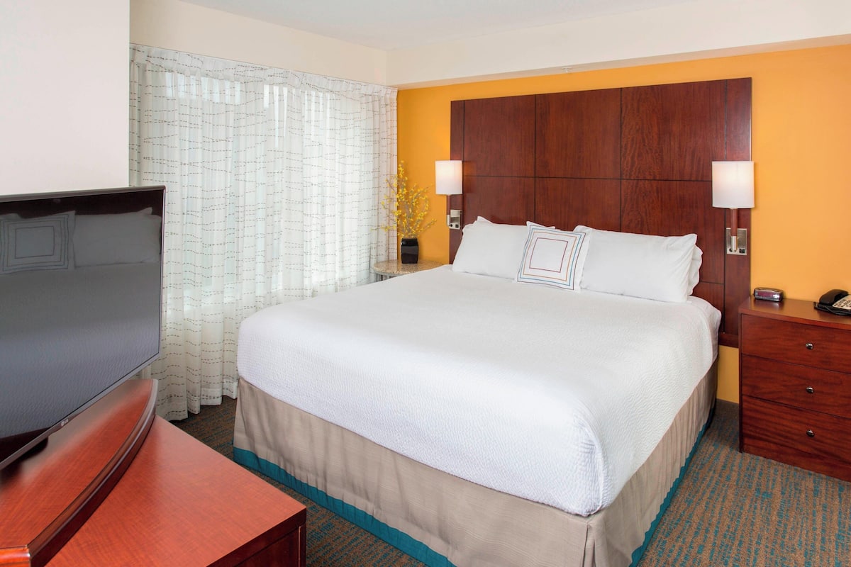 A hotel room with a large bed, a TV, a wooden nightstand, and a lamp.
