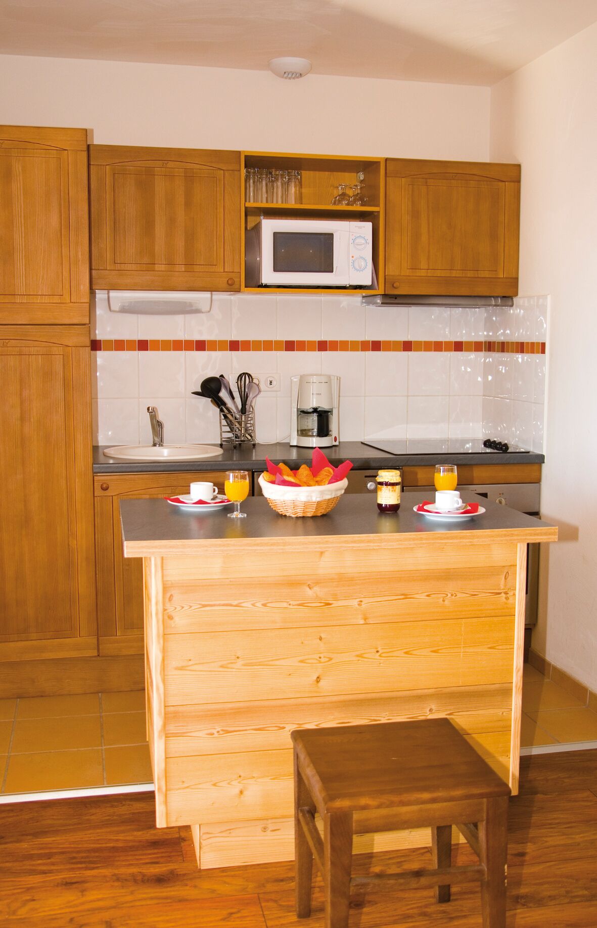 A compact kitchen with wooden cabinets, a microwave, a coffee maker, and a breakfast setup on the counter.