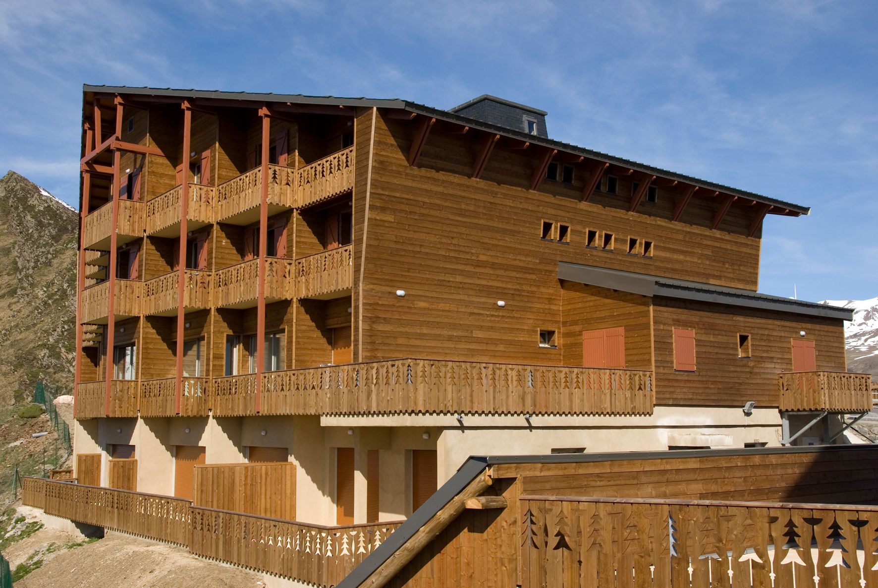 A multi-story wooden building with balconies, a ski lift, and a mountain backdrop.