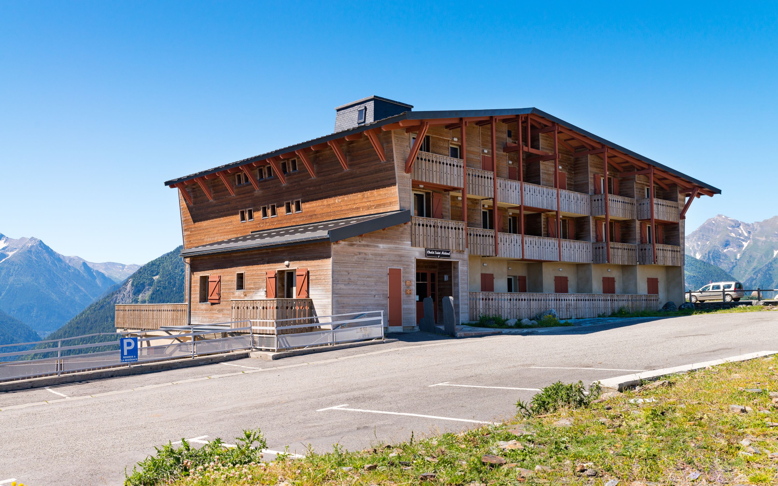 Un immeuble en bois à plusieurs étages, doté de balcons, d’un espace de stationnement et surplombant un paysage montagneux.