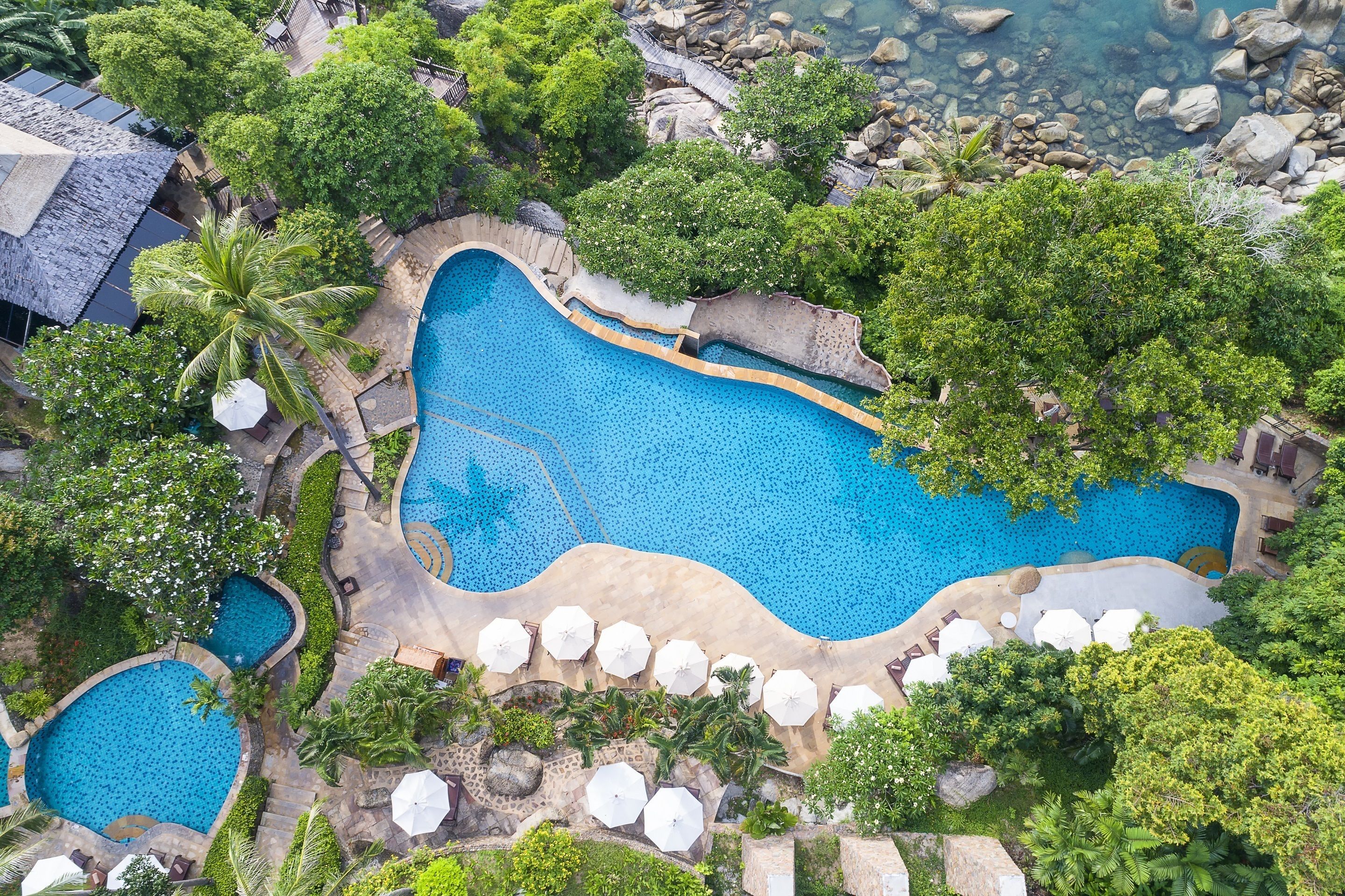 An aerial view of a resort with multiple swimming pools surrounded by lush greenery and palm trees.