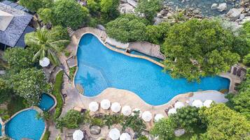 An aerial view of a resort with multiple swimming pools surrounded by lush greenery and palm trees.