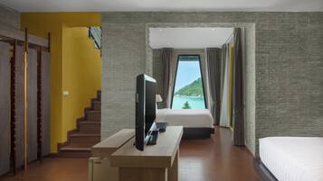 A hotel room with a bed, a TV on a wooden table, a staircase, and a view of a mountain and sea.