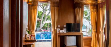 A hotel room with a wooden interior, a television, a small refrigerator, and a view of a swimming pool.