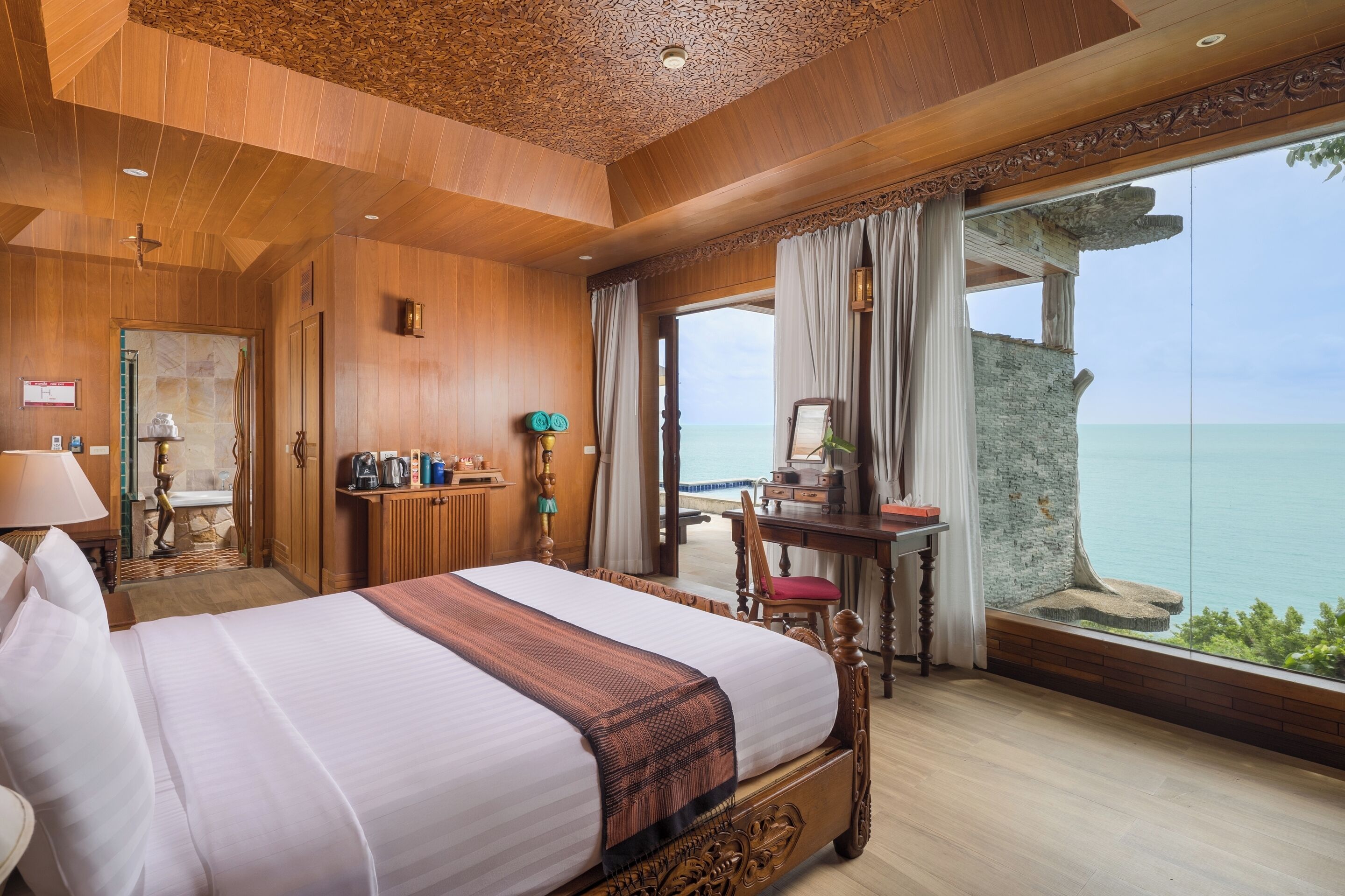 A spacious bedroom with a large bed, wooden ceiling, and a view of the sea.