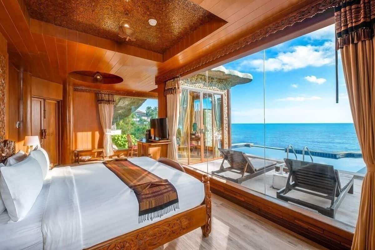 A room with a bed, a TV, a desk, and a balcony with a view of the sea.