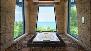 Un baño moderno con una bañera grande, suelo de piedra y amplias ventanas con vistas al mar.