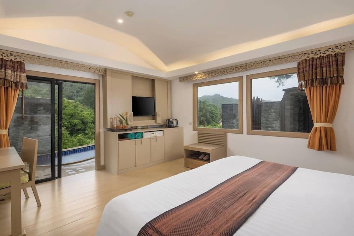 A hotel room with a bed, a desk, a TV, a small kitchenette, and large windows with curtains.