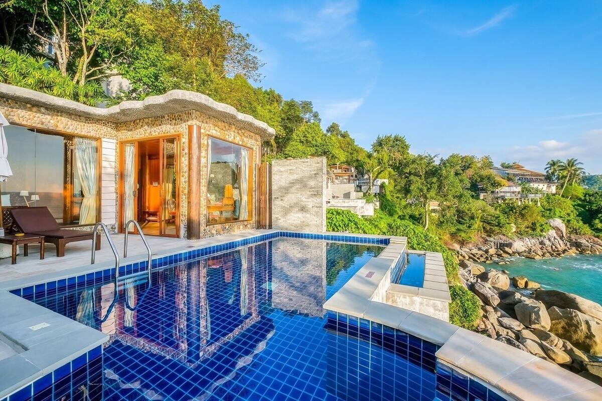 A poolside area with a clear view of the ocean, a lounge chair, and a building with a stone facade.