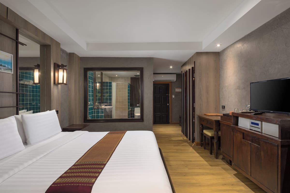 A hotel room with a large bed, a TV, a desk, and a view of the bathroom.