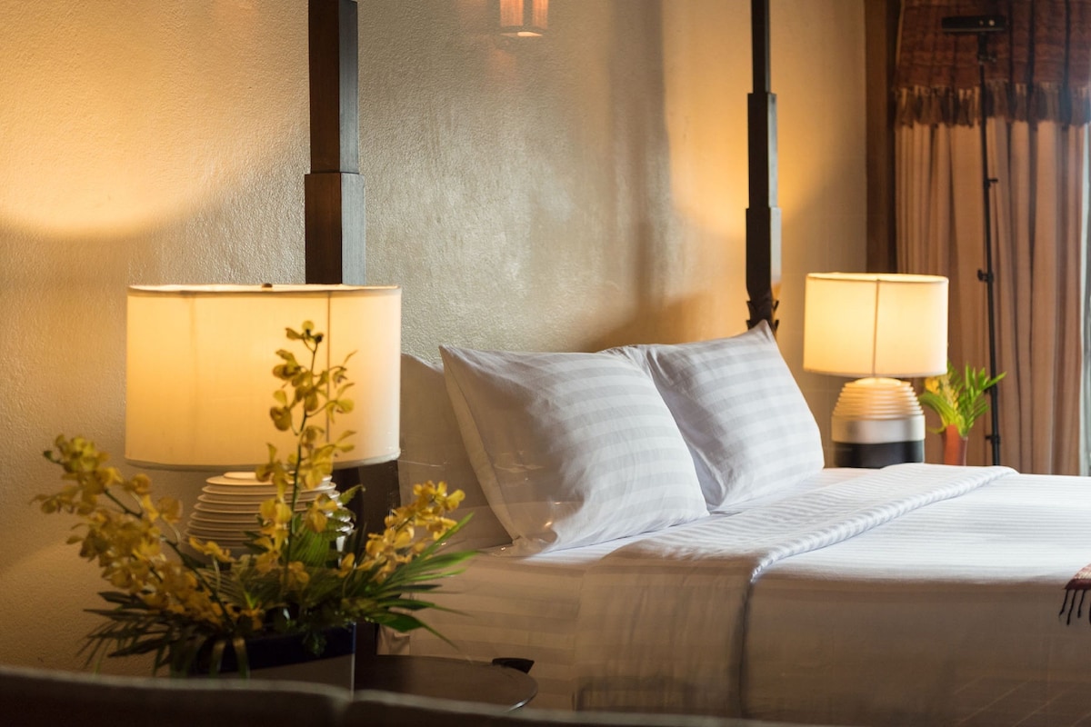 A neatly made bed with white linens and two pillows, flanked by two bedside lamps with white shades.