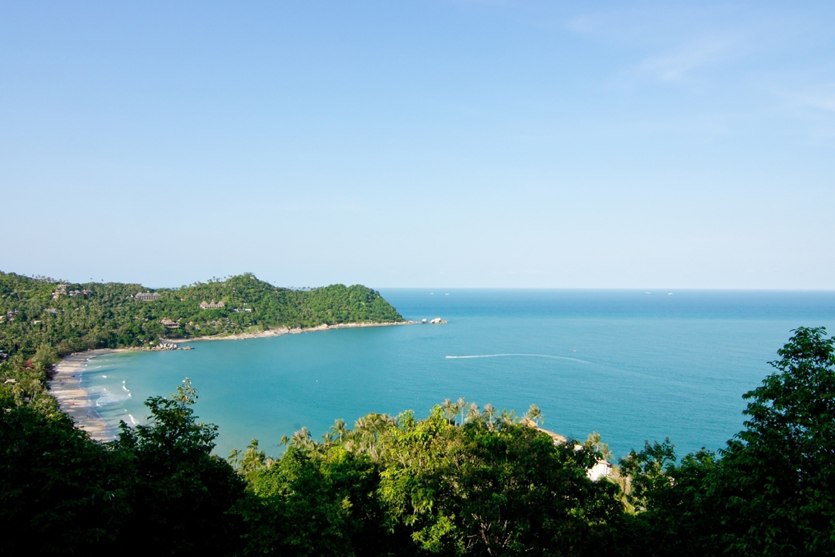 A coastal landscape with a beach, forested hills, and a clear view of the ocean.