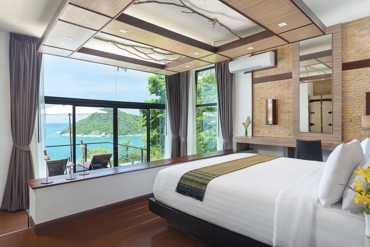 A bedroom with a large bed, a view of the sea, and a balcony with chairs.