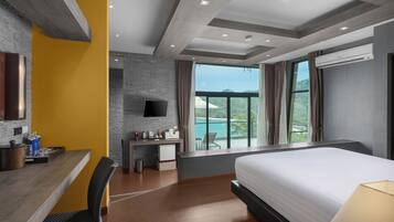 Een moderne hotelkamer met een groot bed, een bureau met stoel, een kleine kitchenette, een flatscreen-tv en een balkon met uitzicht op zee.