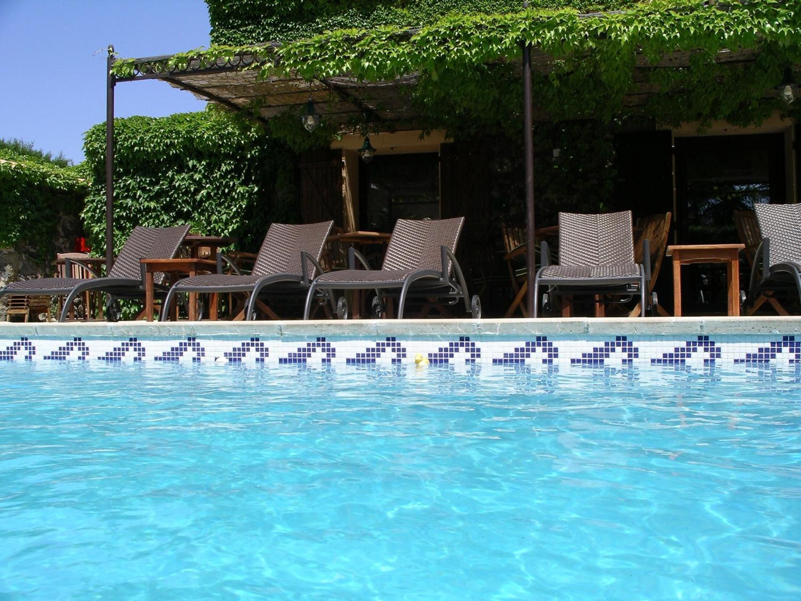 Une piscine à l’eau d’un bleu cristallin, entourée de chaises longues et d’une pergola recouverte de verdure.