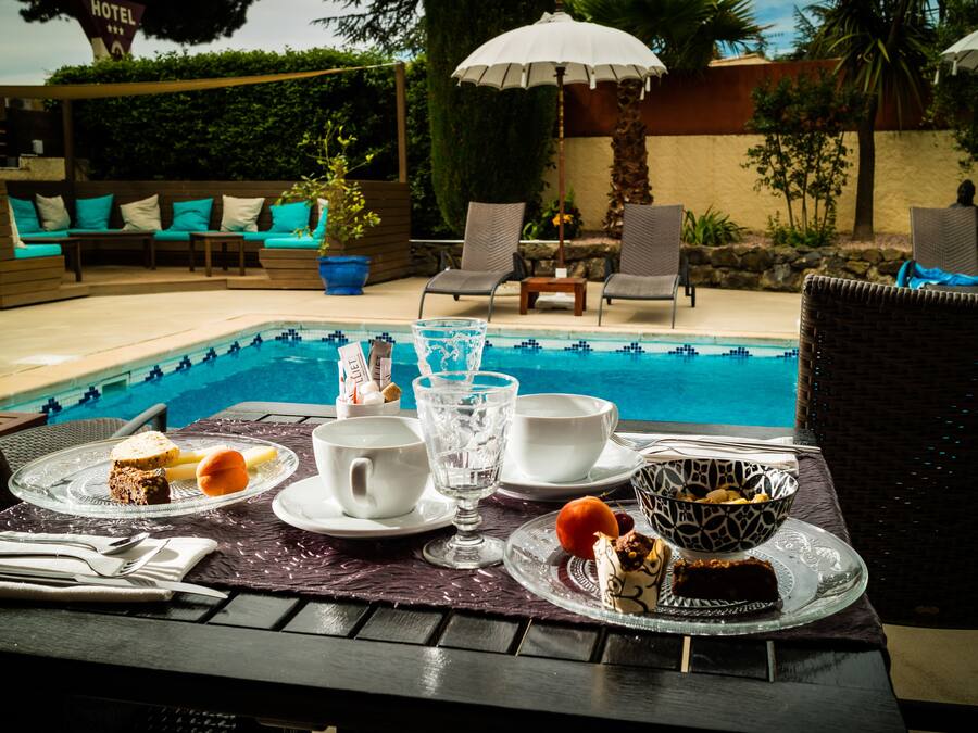 A dining table with a pool view, outdoor seating, and a dessert setup.