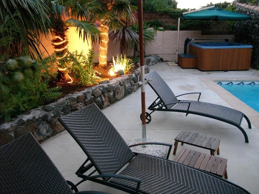 A poolside area with lounge chairs, a hot tub, and a decorative light feature.