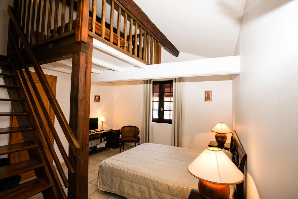 Ein Schlafzimmer mit einer Holztreppe, einem Bett, einem Schreibtisch mit Stuhl und einem Fenster mit Vorhängen.