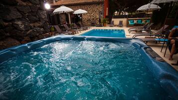 A swimming pool with hot tub, lounge chairs, umbrellas, and a stone wall.