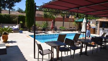 A poolside area with lounge chairs, a table, and a covered seating area.