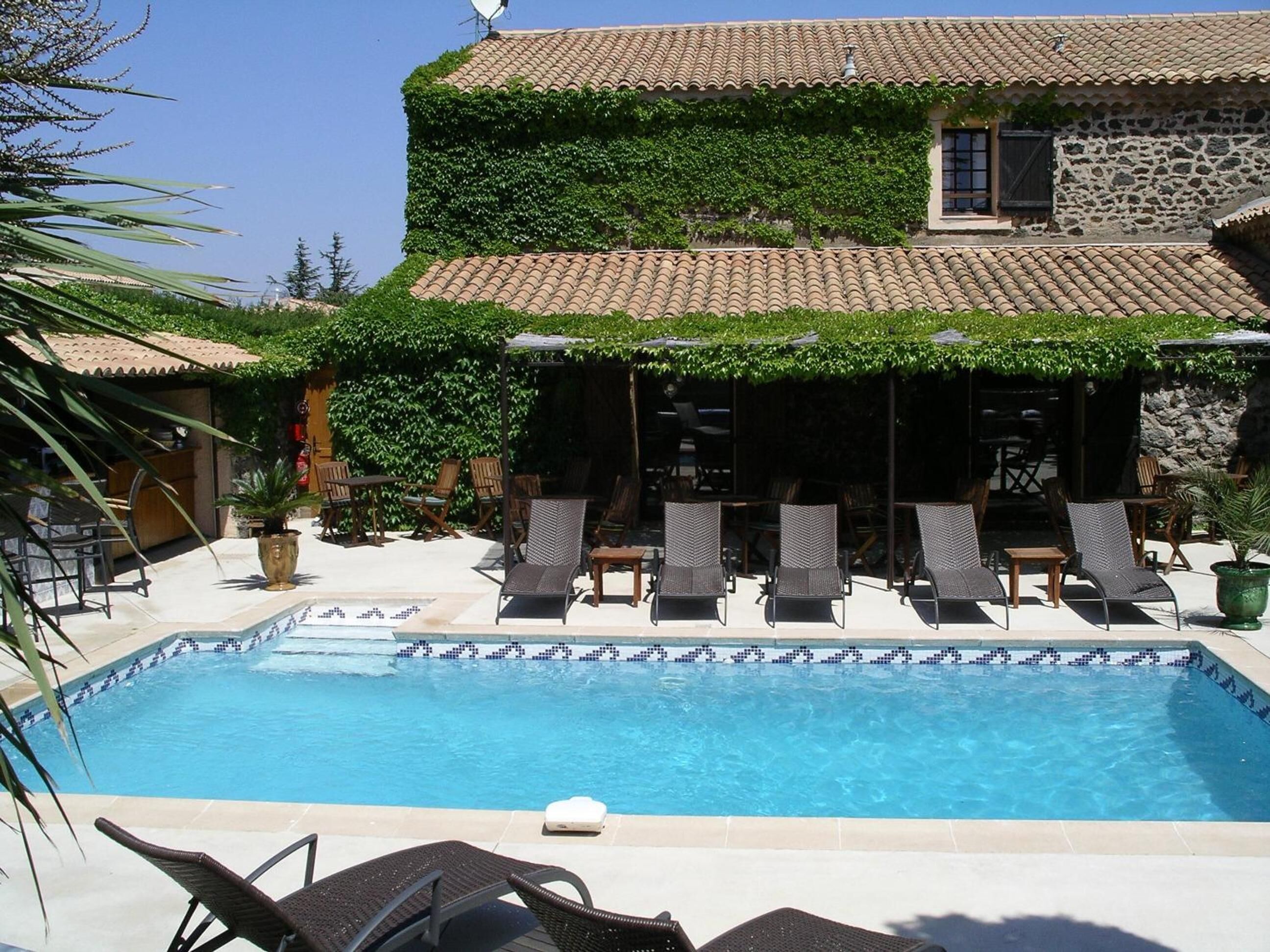 A two-story building with a tiled roof and a swimming pool with lounge chairs.