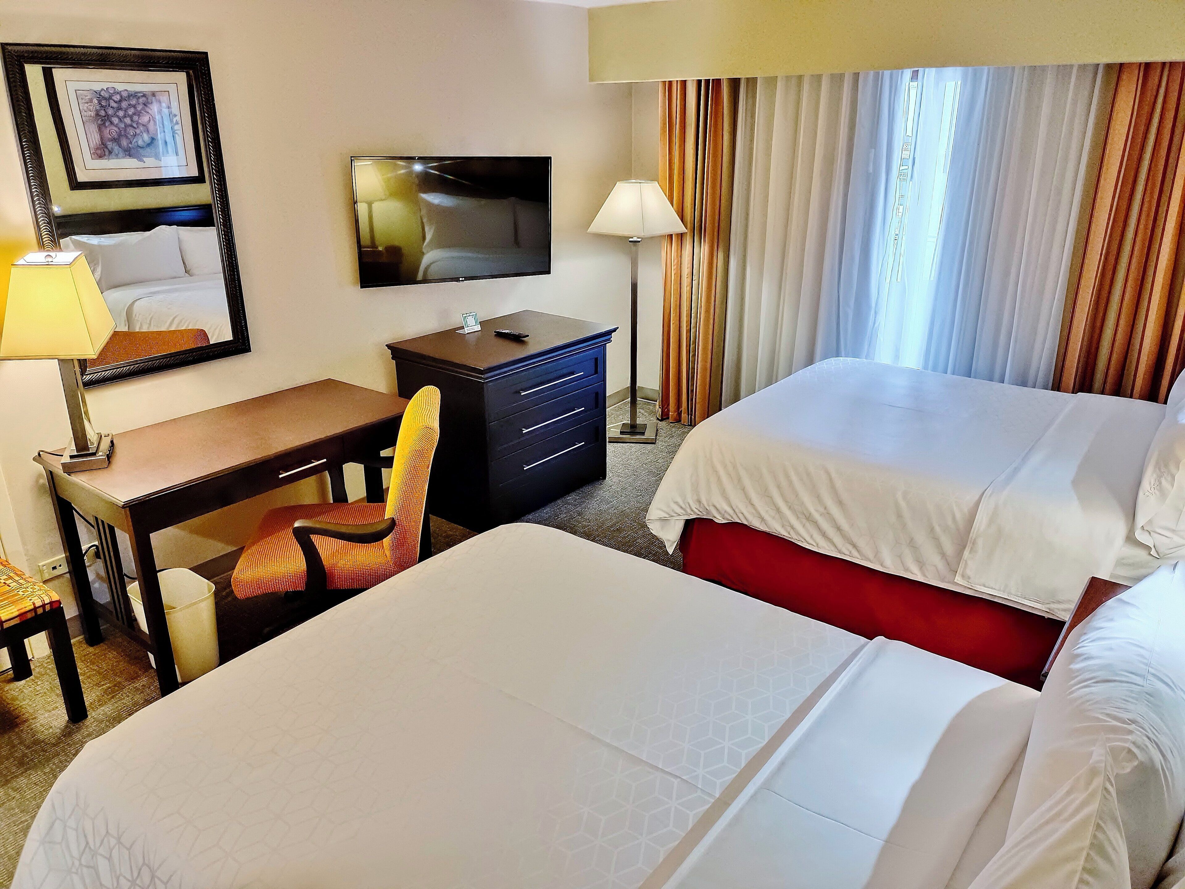 A hotel room with two beds, a desk, a chair, a television, and a window with curtains.