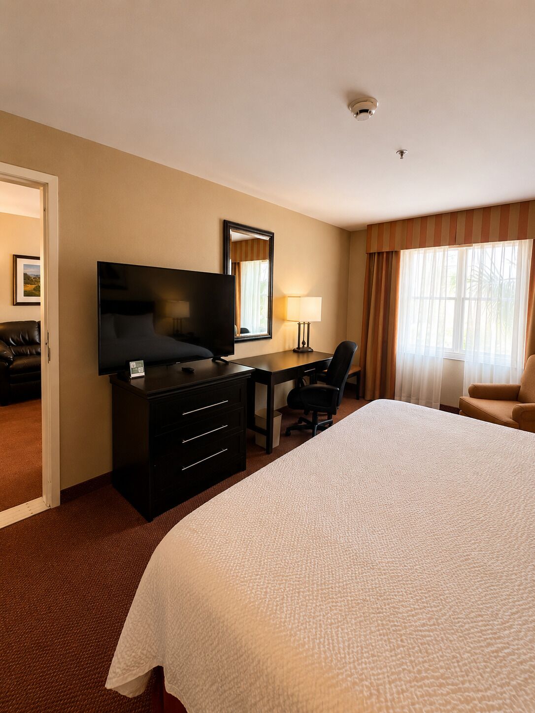 A hotel room with a bed, a desk with a chair, a television, a lamp, and a window with curtains.