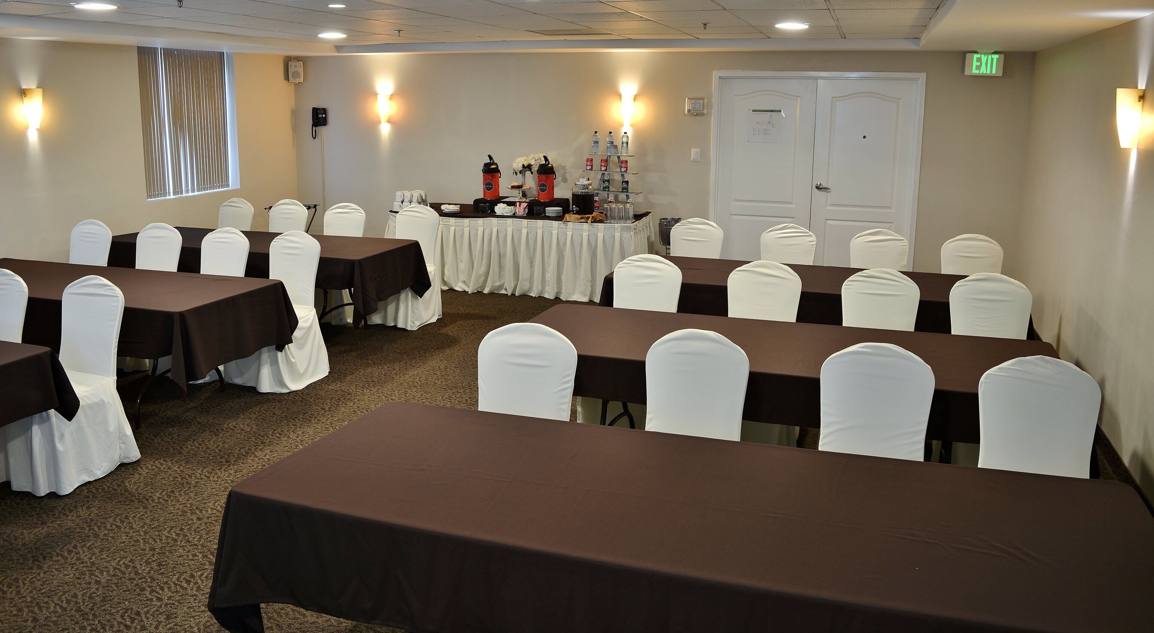Sala de conferências com mesas e cadeiras, mesa de buffet com comida e bebidas, e uma porta de saída.