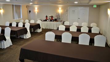Sala de conferências com mesas e cadeiras, mesa de buffet com comida e bebidas, e uma porta de saída.