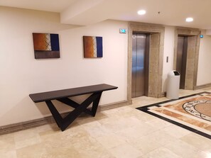 A lobby with a marble floor, a black table, two abstract paintings, an elevator, and a trash bin. - Holiday Inn Reynosa Zona Dorada by IHG (Reynosa)