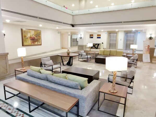 A spacious lobby with a grey sofa, a wooden bench, and a coffee table. There are multiple lamps and a large painting on the wall. - Holiday Inn Reynosa Zona Dorada by IHG (Reynosa)