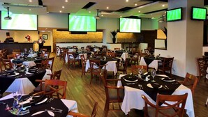 A restaurant with multiple tables, chairs, and sports screens displaying a soccer game. - Holiday Inn Reynosa Zona Dorada by IHG (Reynosa)