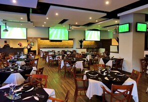 A restaurant with multiple tables, chairs, and sports screens displaying a soccer game. - Holiday Inn Reynosa Zona Dorada by IHG (Reynosa)