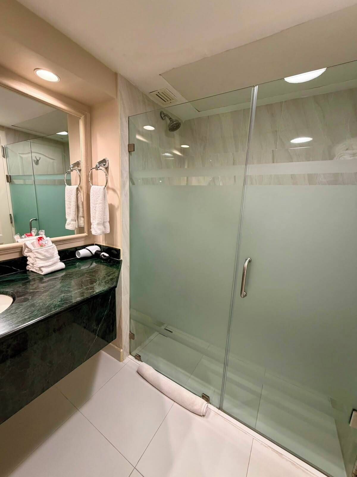 Un baño moderno con cabina de ducha de vidrio, encimera de mármol y un espejo grande.
