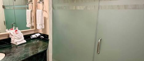 Un baño moderno con cabina de ducha de vidrio, encimera de mármol y un espejo grande.