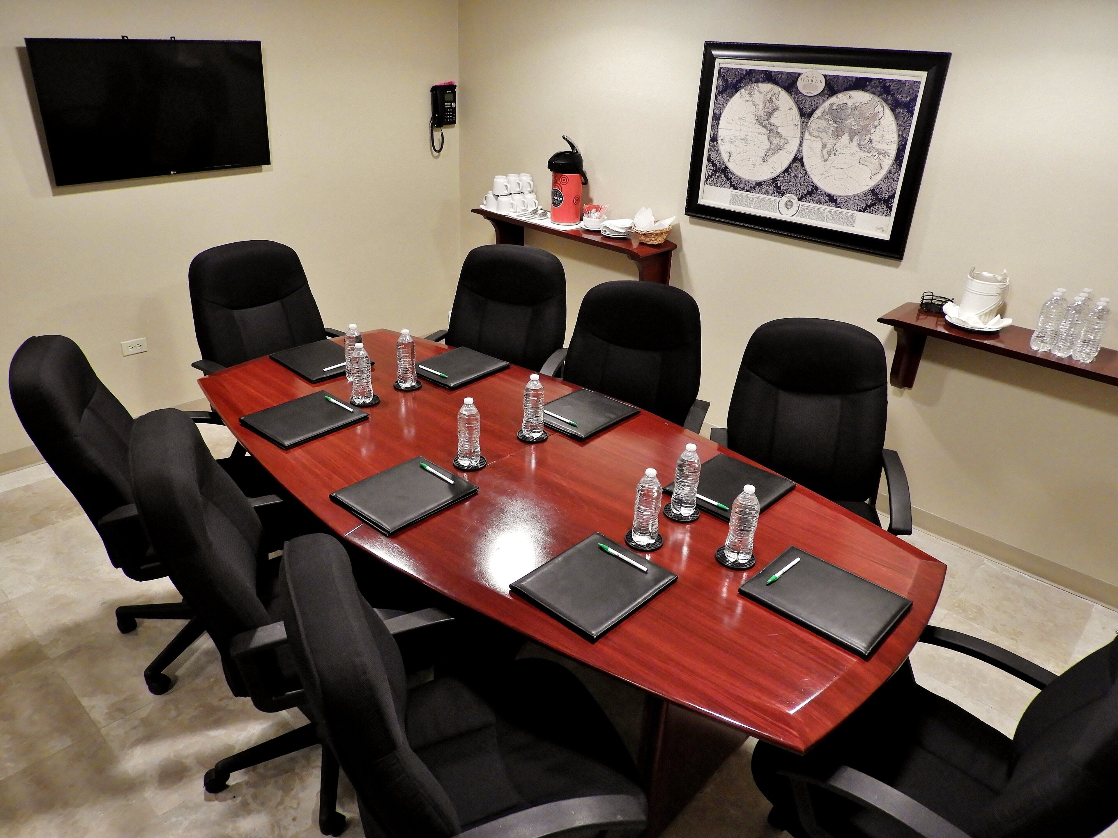 A conference room with a long table, black chairs, water bottles, and a framed world map on the wall.
