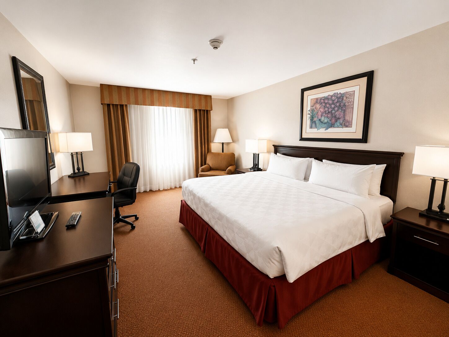 Een hotelkamer met een groot bed, een bureau met een televisie, een stoel en een nachtkastje met een lamp.