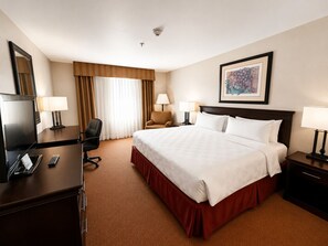 Habitación de hotel con una cama grande, un escritorio con televisor, una silla y una mesita de noche con lámpara.
