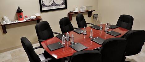 Un salón de conferencias con una mesa redonda, sillas negras, botellas de agua y un mapa mundial enmarcado en la pared.