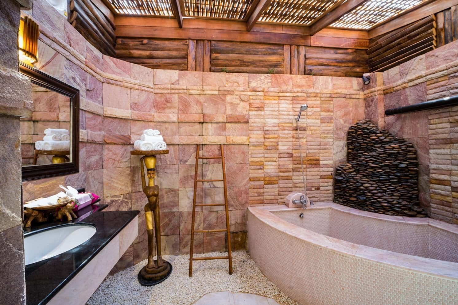 A bathroom with a stone wall, a bathtub, a vanity with a mirror, and a golden statue.