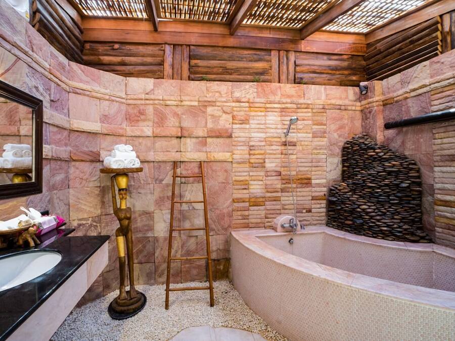 A bathroom with a stone wall, a bathtub, a vanity with a mirror, and a golden statue.