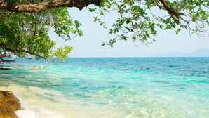 A beach with clear turquoise water, a rocky shoreline, and a tree branch overhead. - Santhiya Koh Chang Resort (Ko Chang)