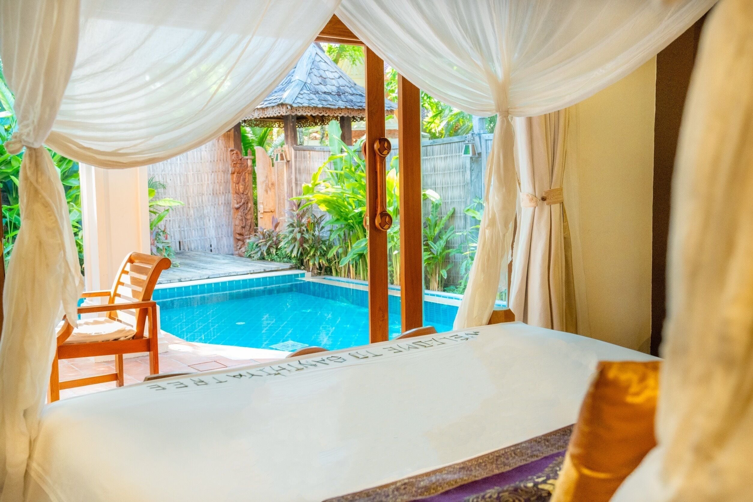 Ein Zimmer mit einem Bett, Blick auf einen Swimmingpool und einem Holzstuhl.