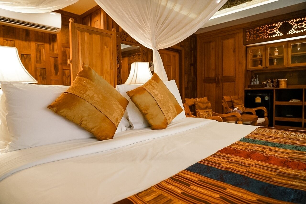 A bed with white linens and two decorative pillows, a canopy overhead, and a wooden cabinet with glass doors in the background.