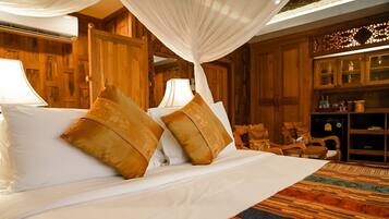 A bed with white linens and two decorative pillows, a canopy overhead, and a wooden cabinet with glass doors in the background.