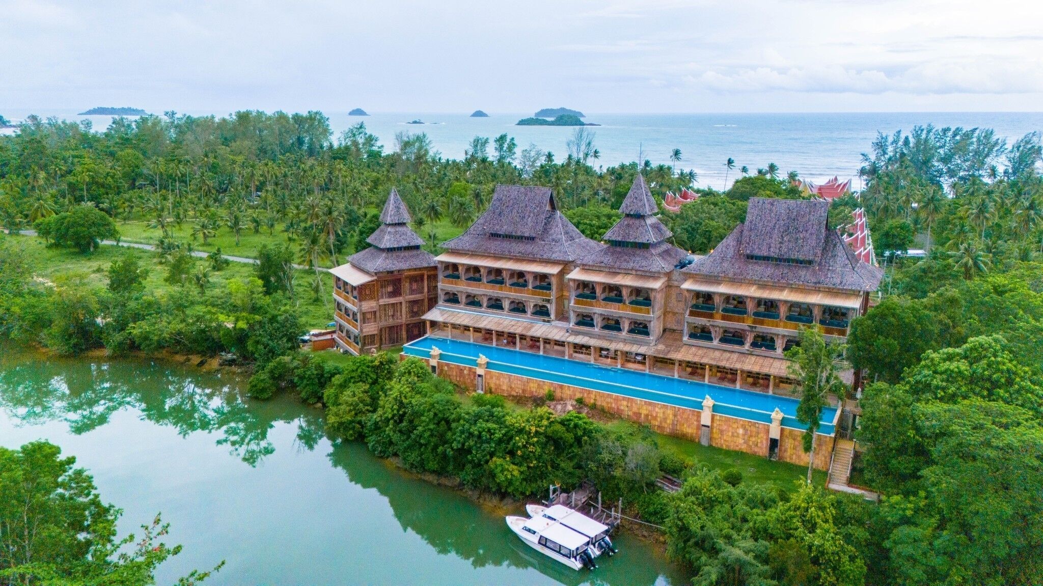 Ein großes Resort mit mehreren Gebäuden, einem Schwimmbad und einem Boot, das in der Nähe des Wassers liegt.