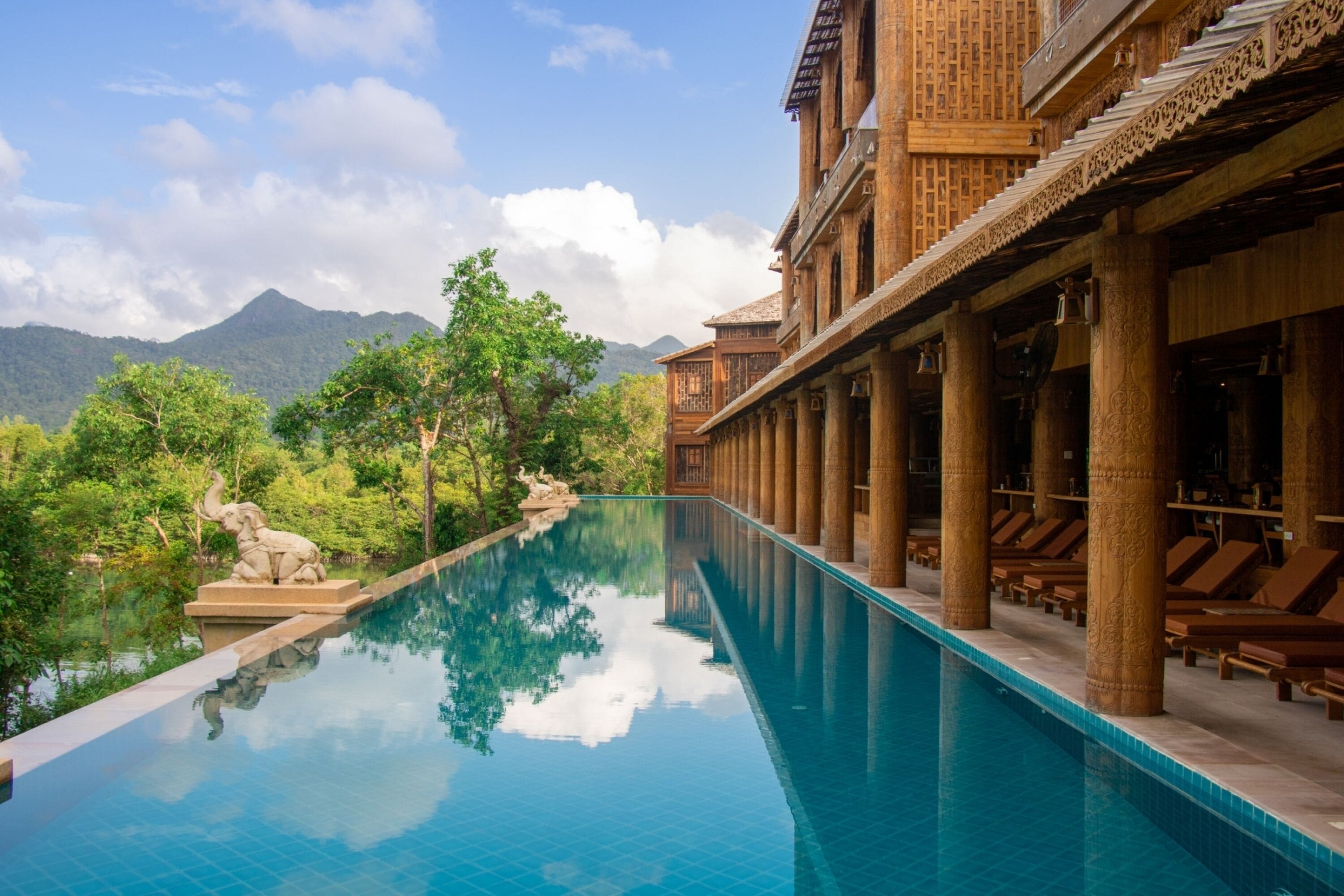 A pool with a clear view of mountains in the background, surrounded by lush greenery and traditional architecture.